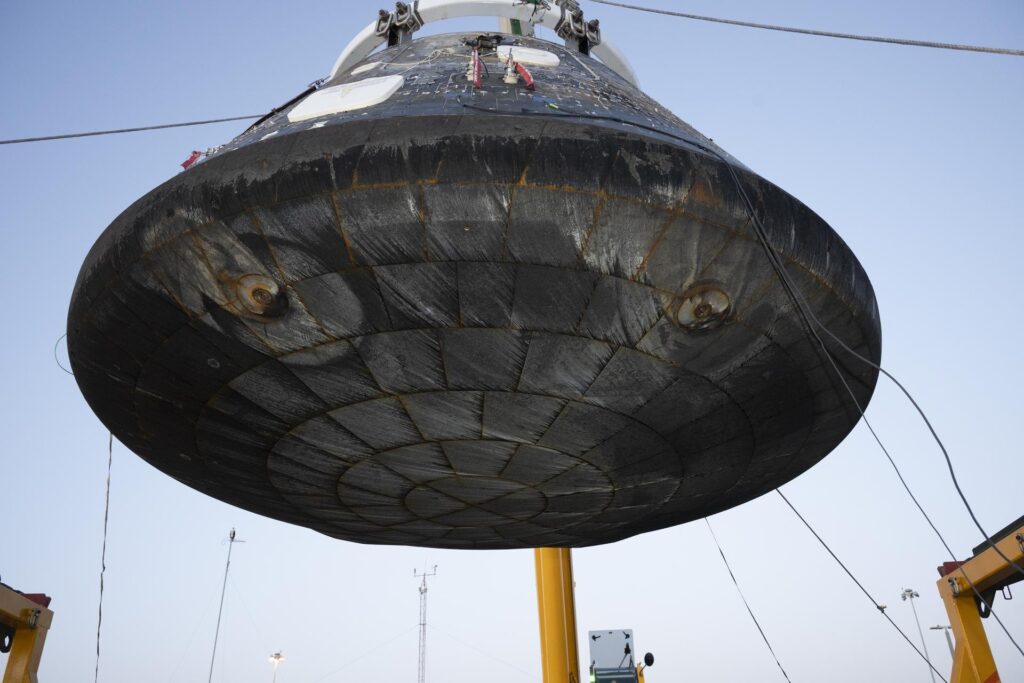 The Artemis II Orion crew module lifted for inspection, showing the heat shield's recessed and concentric patterns