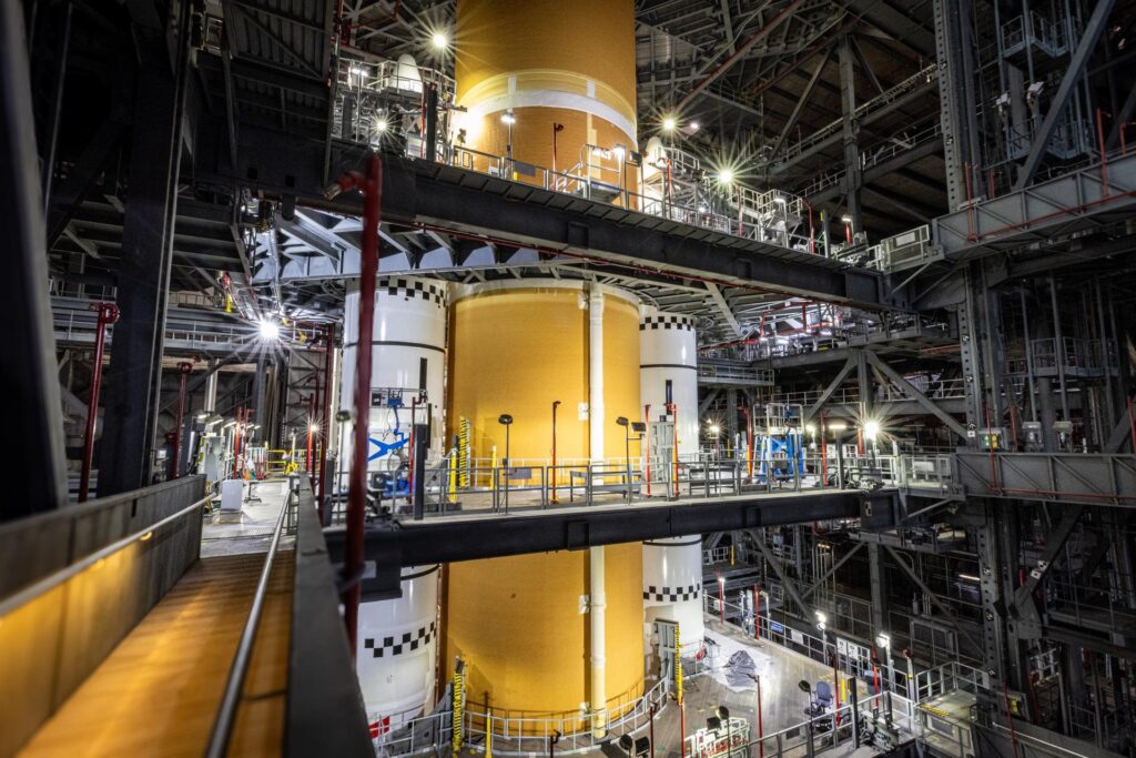 The SLS core stage flanked by the nose cones of the two solid rocket boosters inside the Vehicle Assembly Building
