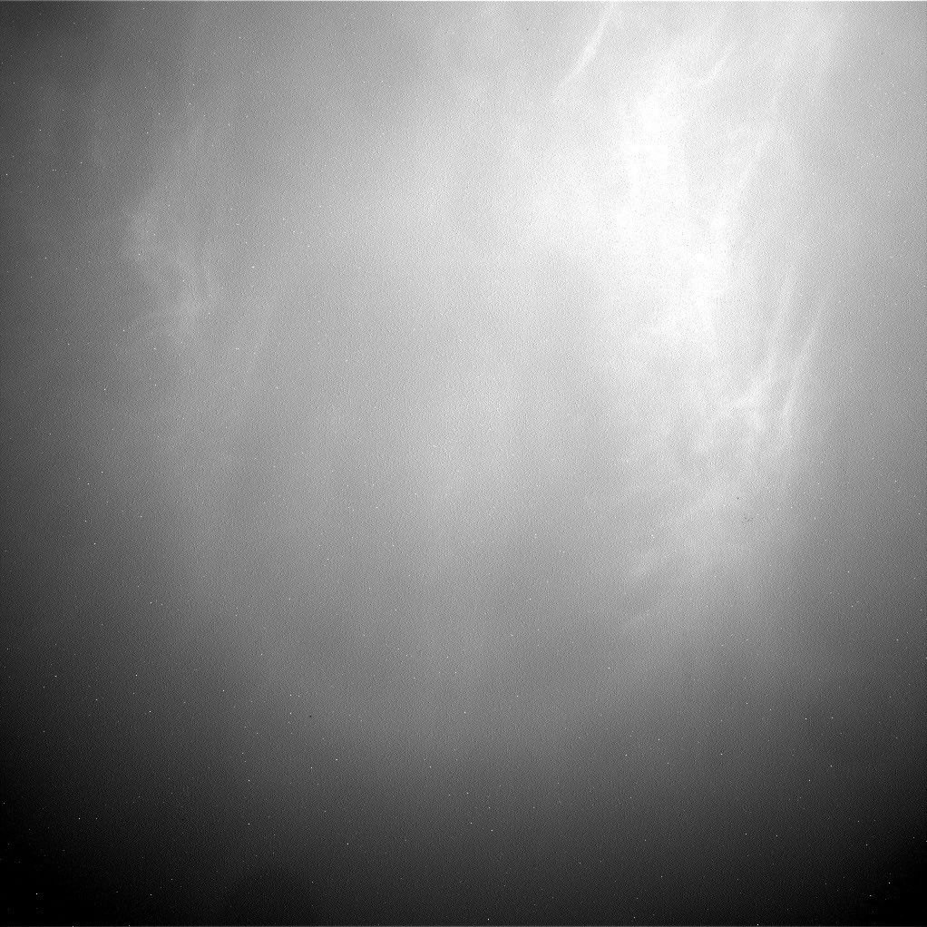 Grainy black-and-white Navcam view of the Martian sky with wispy, cirrus-like twilight clouds lit in the upper right