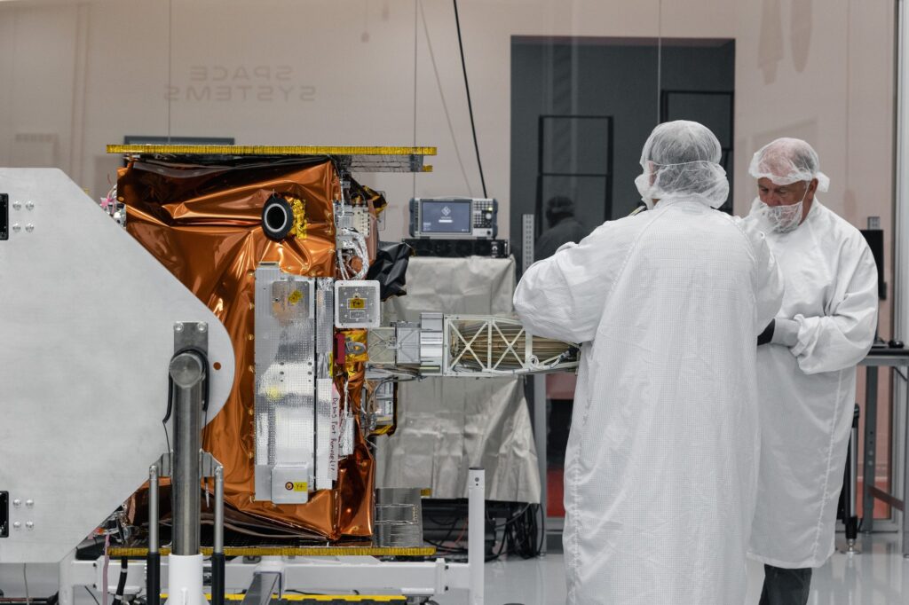 Technicians in cleanroom garments work on Viasat's Maxwell payload, wrapped in gold thermal insulation, in Long Beach, California