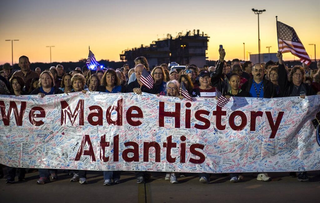 Staff carry a signed banner beside the shuttle Atlantis during its move to the Kennedy Space Center Visitor Complex
