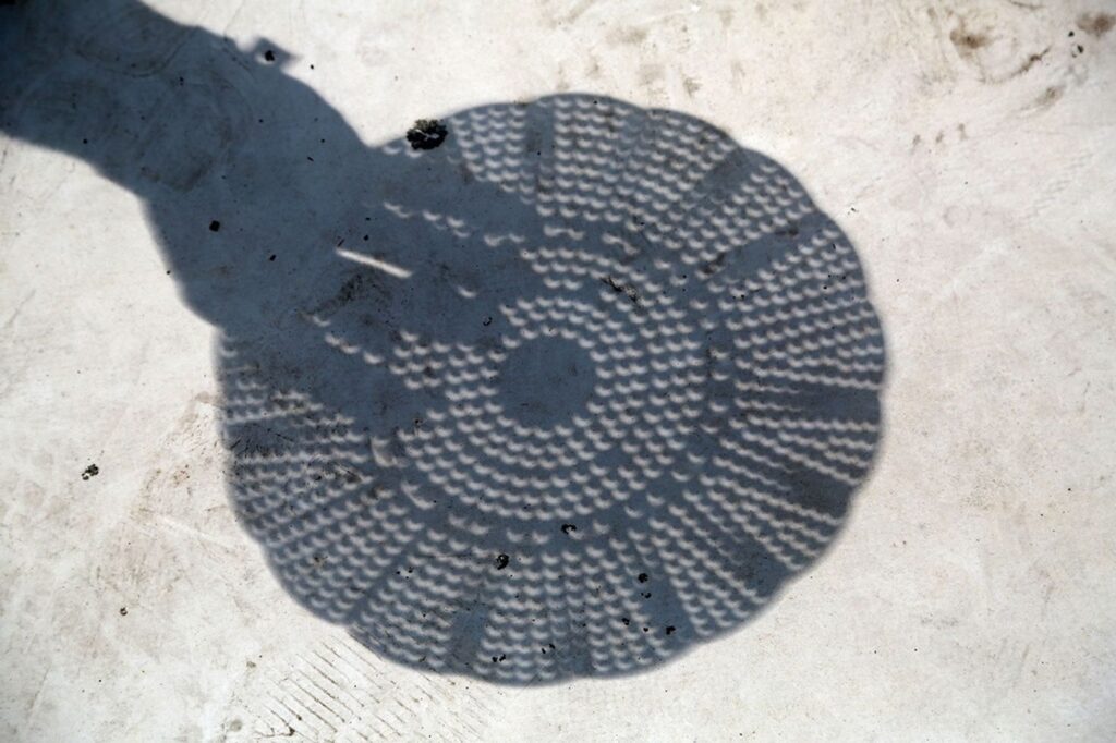 A hand holding a kitchen colander that casts crescent-shaped Sun images onto a surface