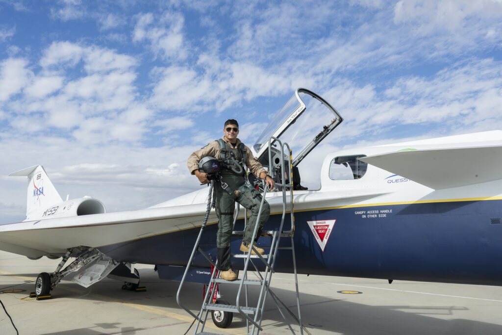 NASA test pilot Mike Lippert standing on a ladder beside the X-59 with the cockpit open, helmet under his arm